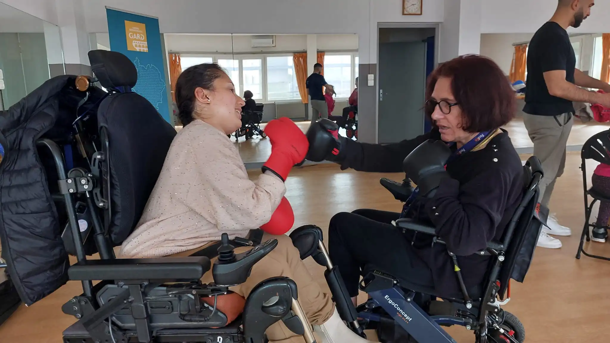 Deux personnes en fauteuil roulant essayant la boxe grâce à l'aide de bénévoles