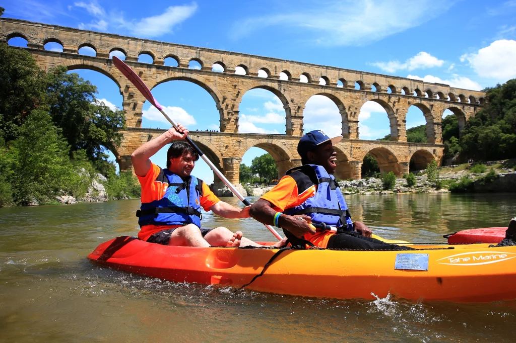 deux hommes handisport sur un canoë sur une rivière en face du pond du Gard